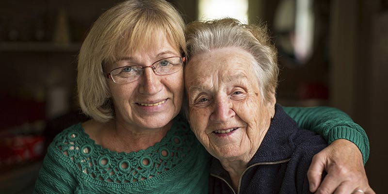 Older woman hugging her elderly mother smiling.