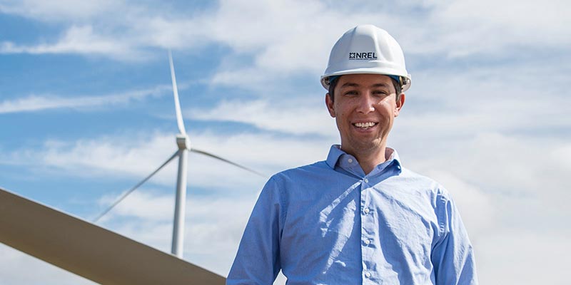 Man wearing a hard hat, standing in front of a wind turbine.