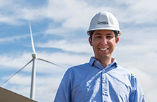 Man wearing a hard hat, standing in front of a wind turbine.