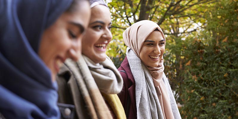 Young Muslim women walking together through the park, smiling and laughing.