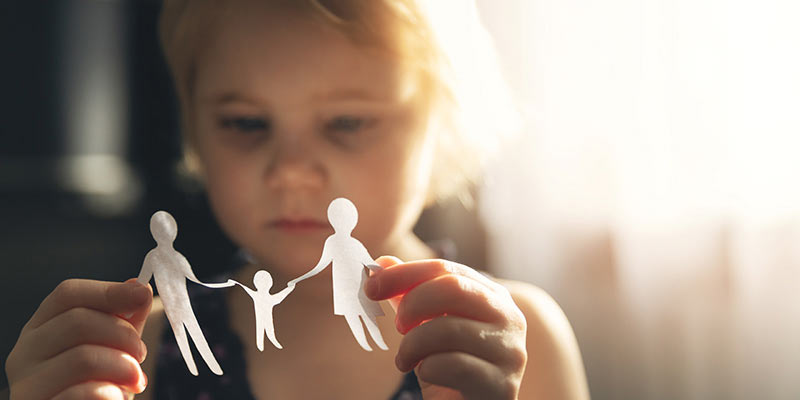 Young child looking at a paper cut-out of parents holding their child's hands.