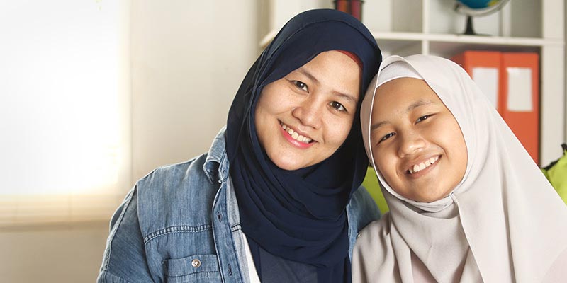 Muslim mother and daughter indoors smiling at camera.