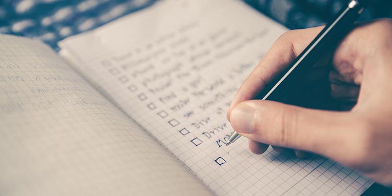 Close up of person writing a checklist on a notepad.