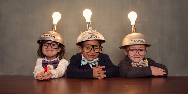 Three young smiling kids wearing "thinking caps" with a lightbulb on top.