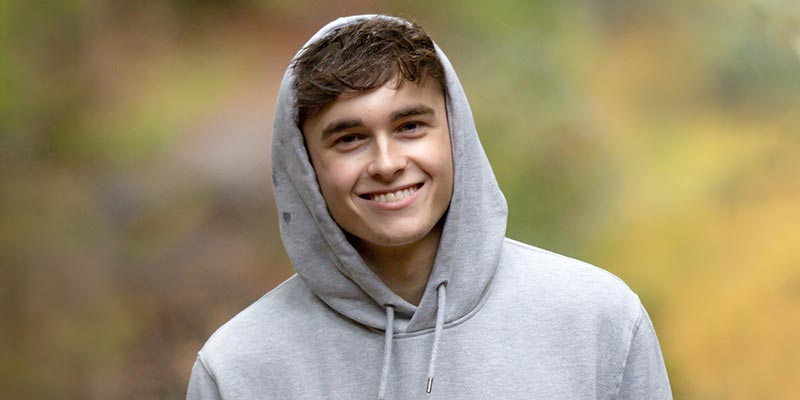 Teenage boy standing outdoors smiling at camera.