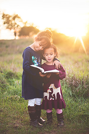 Young sisters reading bible in a field of grass